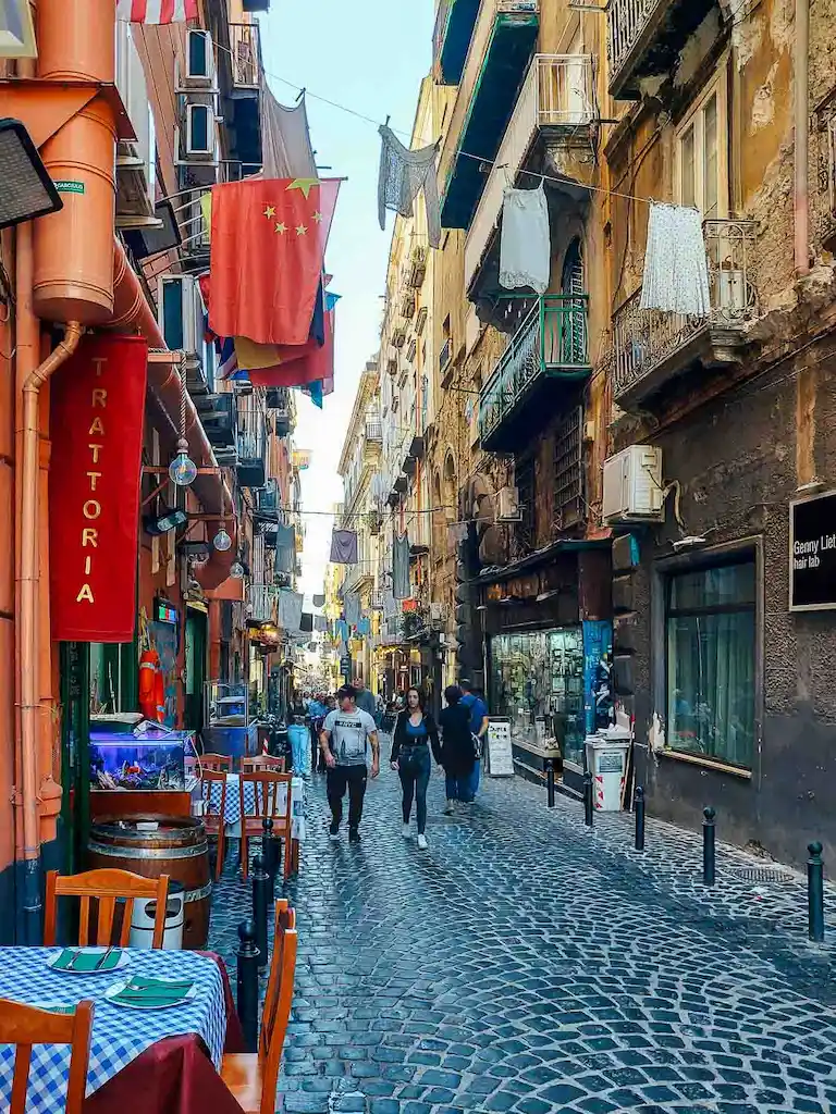 The historic center of Naples with clothes hanging by the balconies and typical italian tables on the side of the street restaurants
